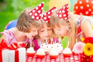Kids blowing out candles on a cake at a birthday party.