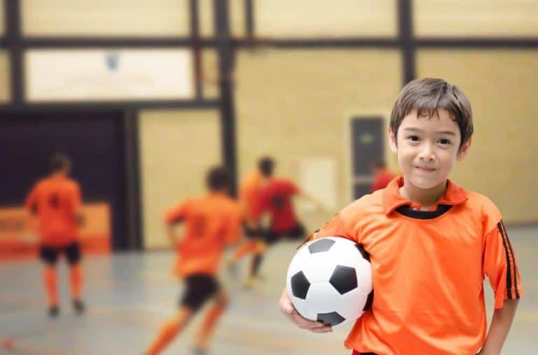 A boy holding a ball while kids behind him play an indoor Smoky Mountain soccer tournament.