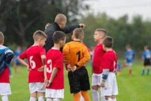A coach giving direction to a group of boys playing soccer.