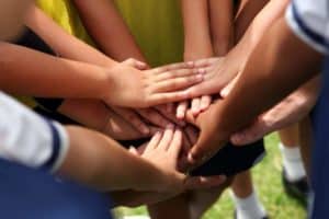 A group of kids on a Smoky Mountain sports team putting their hands in together,