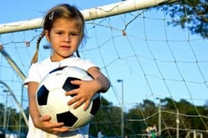 Little girl holding a soccer ball inside of a net.