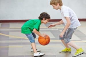 Two boys playing basketball indoors.