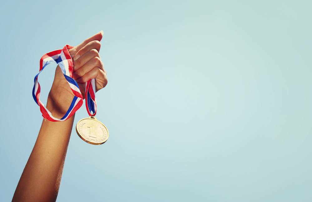 A woman's hand raising a gold medal in the air.