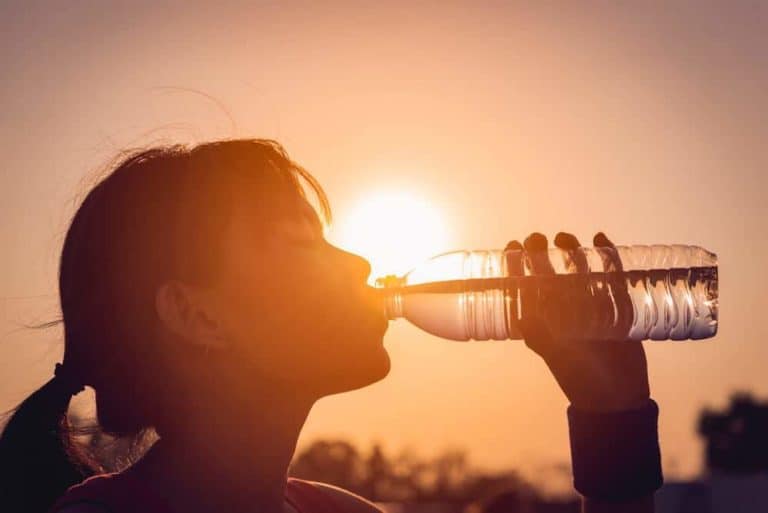 Young woman drinking water with the sun in the background.