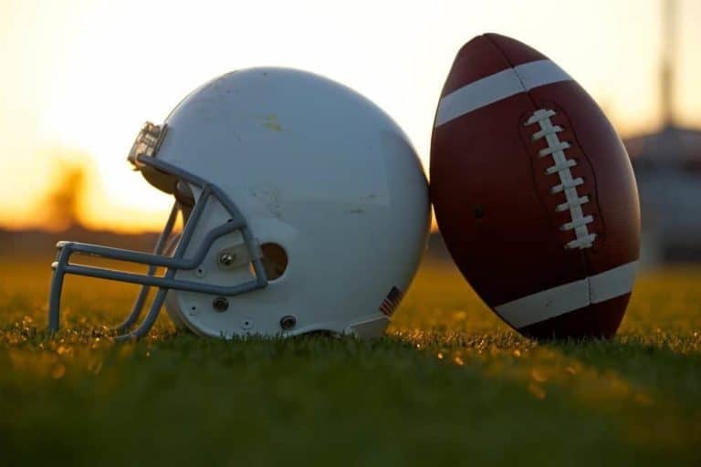 A football and a helmet on a field at sunset.