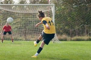 A young woman kicking a soccer ball towards the goal.