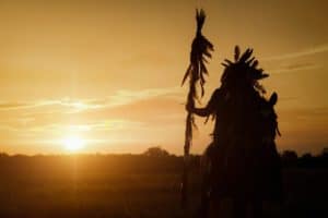 A Native American man riding a horse at sunset.