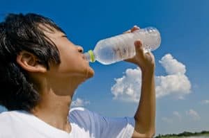 A teenage boy drinking a bottle of water.