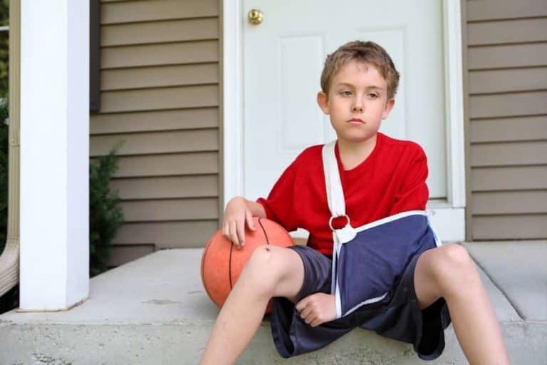 A boy wearing a sling with a basketball on his front steps.