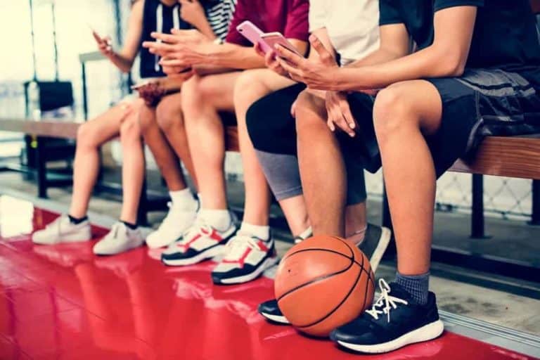 A group of teenage basketball players with smartphones.
