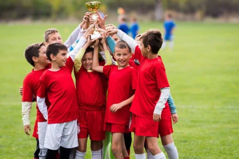 A group of boys on a soccer team hoisting a trophy in the air.